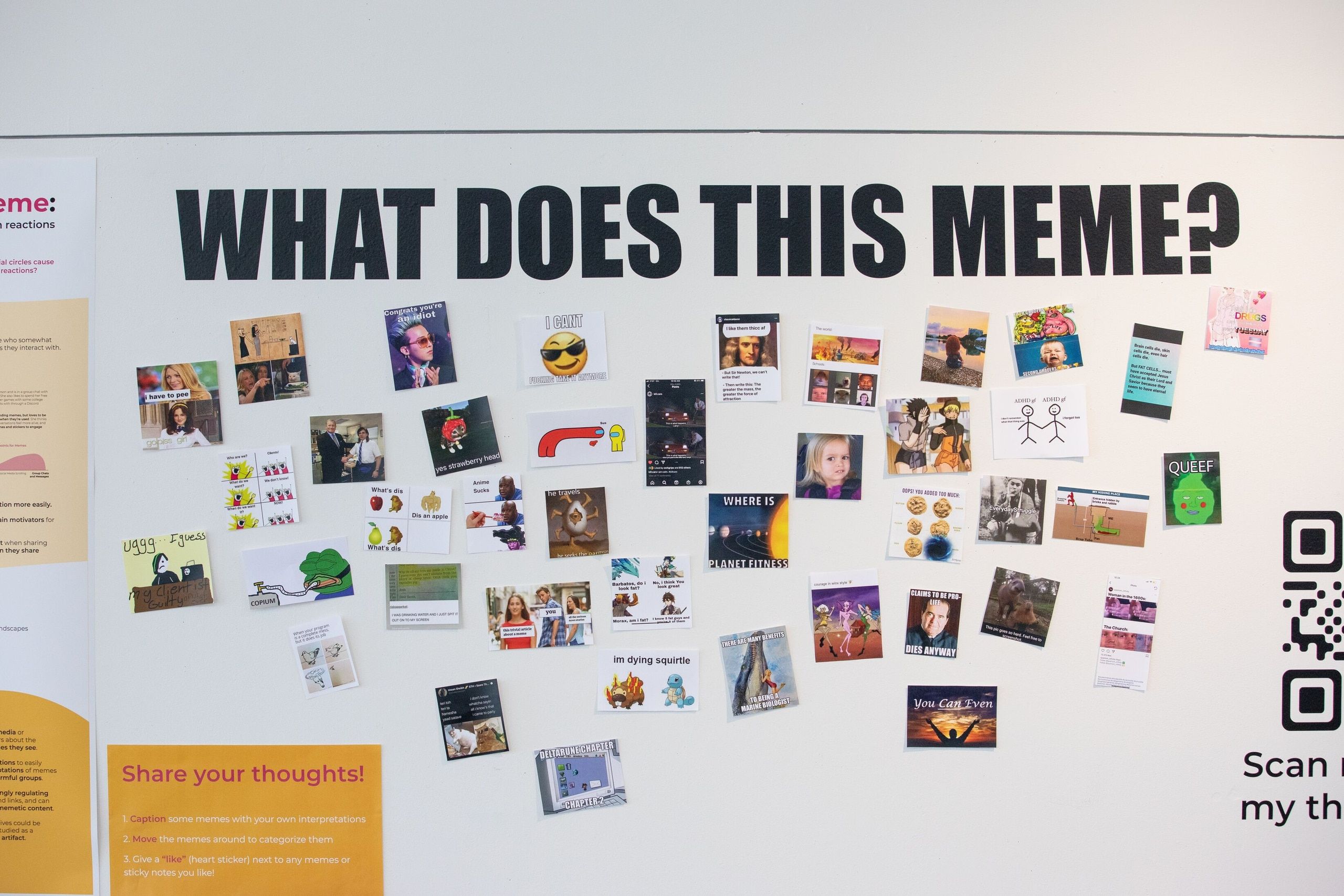 An interactive gallery installation with the heading 'WHAT DOES THIS MEME?' displays dozens of printed images and memes pinned to a white wall, with a QR code for viewer engagement.