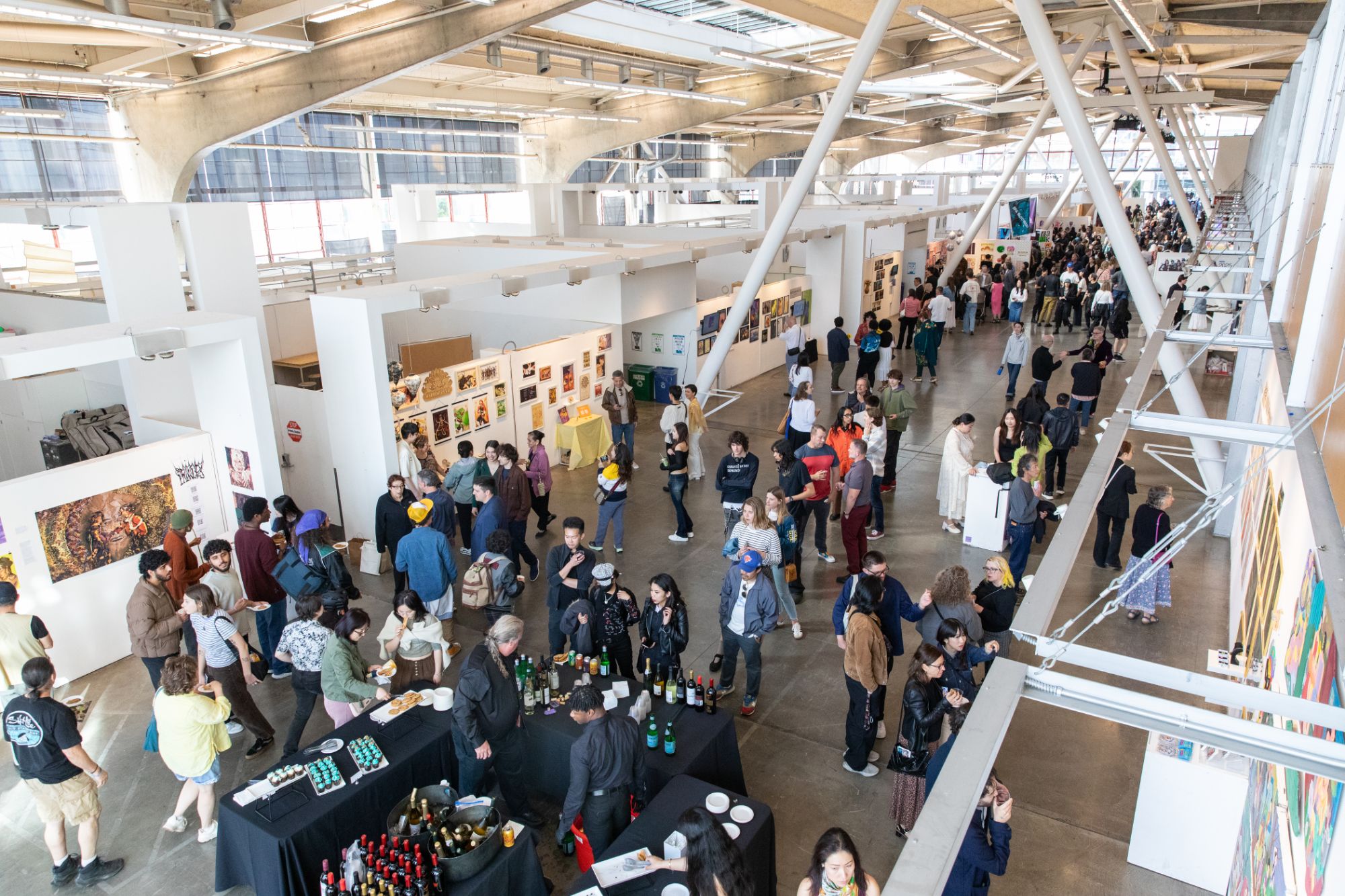 An overhead view of the packed BFA Illustration Senior Show opening reception, with guests mingling around a central drinks table and illustration work covering every wall.