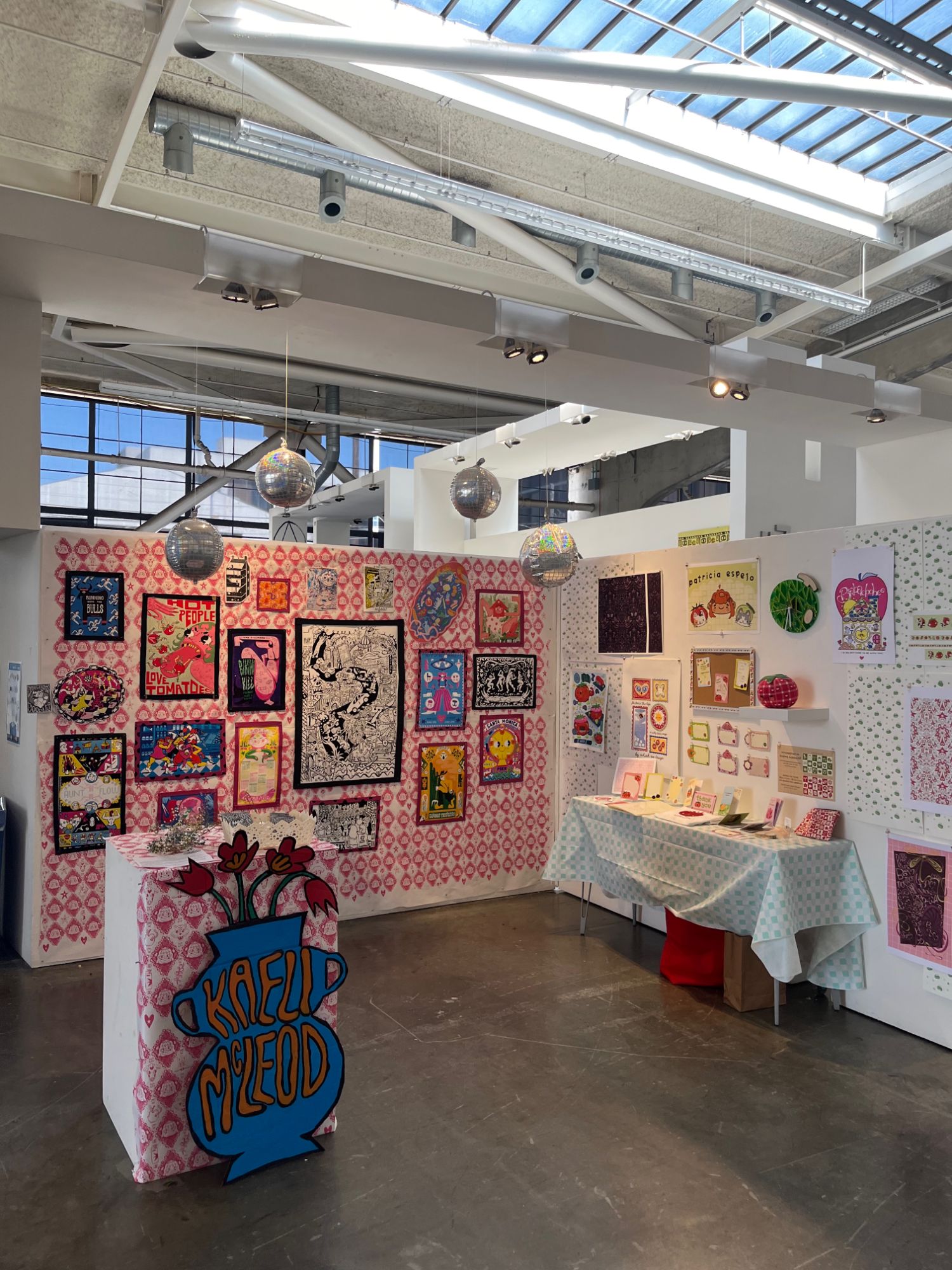 Kaeli McLeod's illustrated booth at the BFA Illustration Senior Show features pink patterned wallpaper, framed prints, disco balls, and a hand-lettered display pedestal.