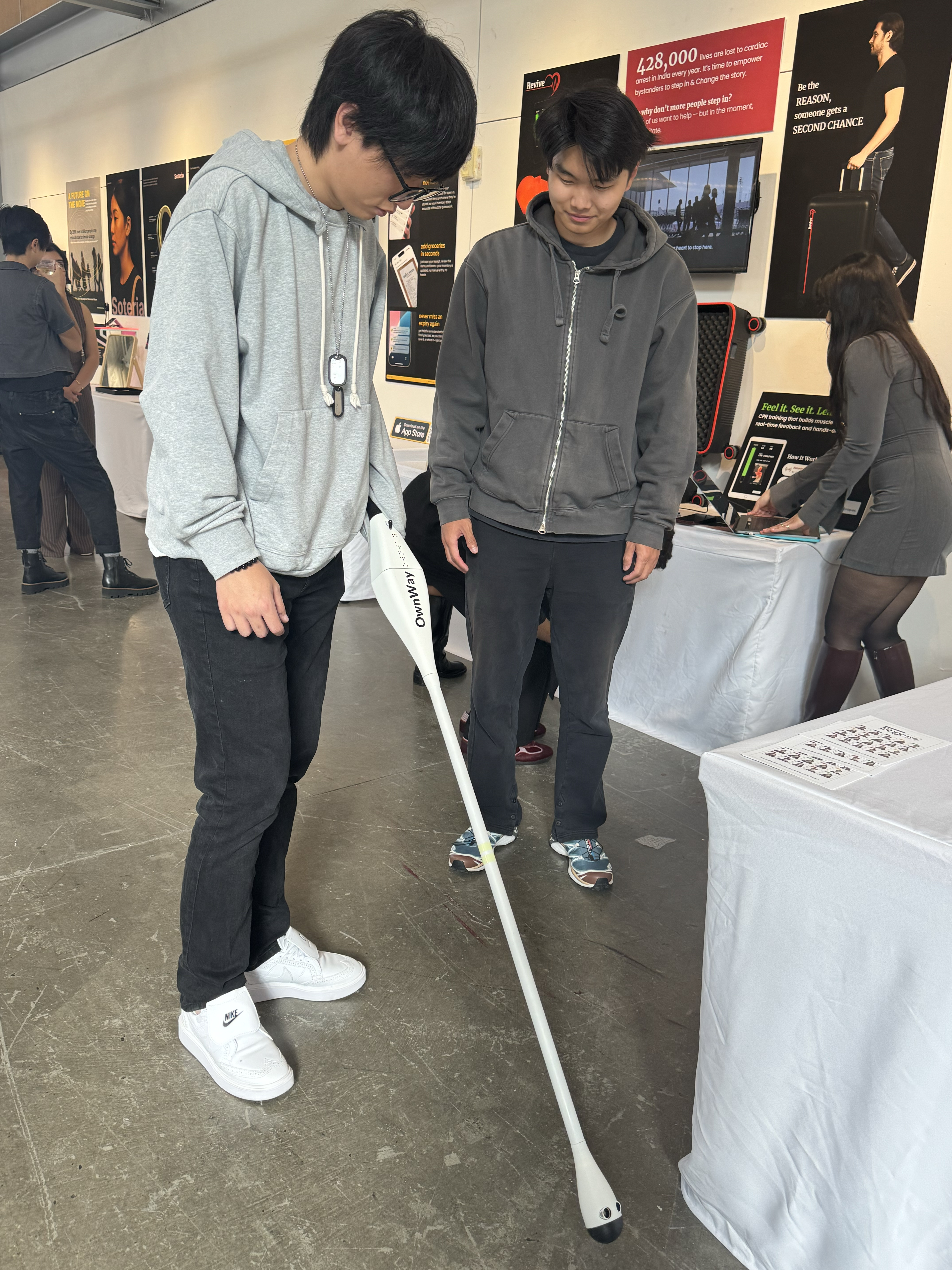 Visitors browse student thesis projects at the BFA Interaction Design showcase, with the OwnWay accessibility cane and Soteria health projects on display.
